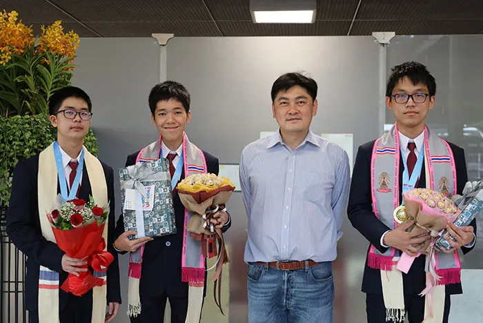 ภาพผู้สอนกับนักเรียนสามคน ถือช่อดอกไม้และของที่ระลึก